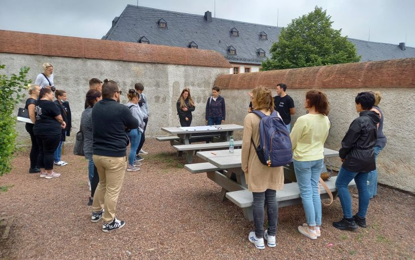 Eine Gruppe steht draußen gemeinsam im Kreis vor einer Mauer.