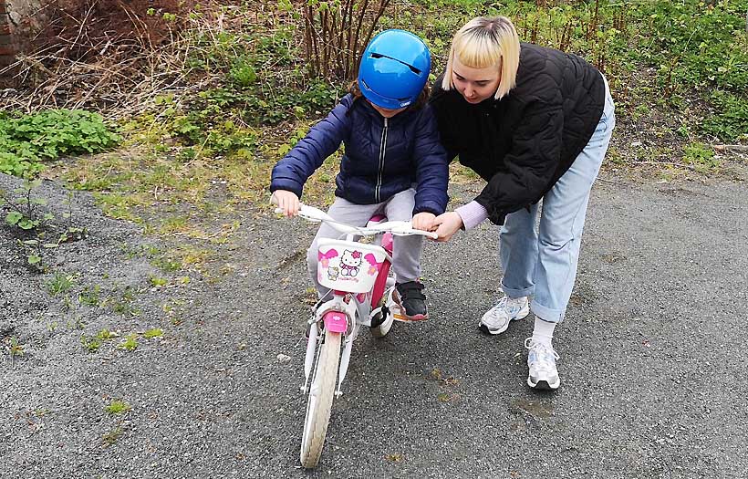 Eine Erzieherschülerin der DPFA Leipzig hilft einem Kind beim Fahradfahren.