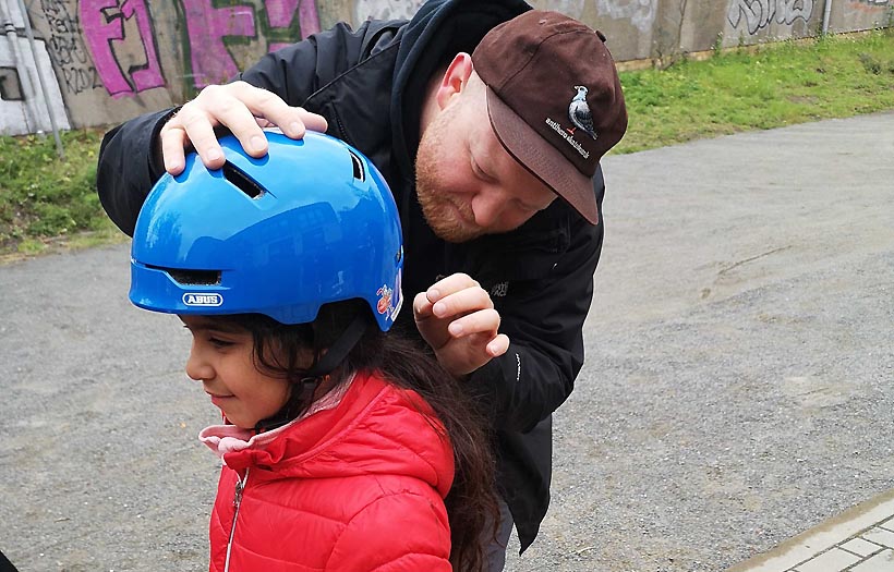 Ein Erzieherschüler der DPFA Leipzig hilft einem Kind den Fahrradhelm korrekt aufzusetzen.