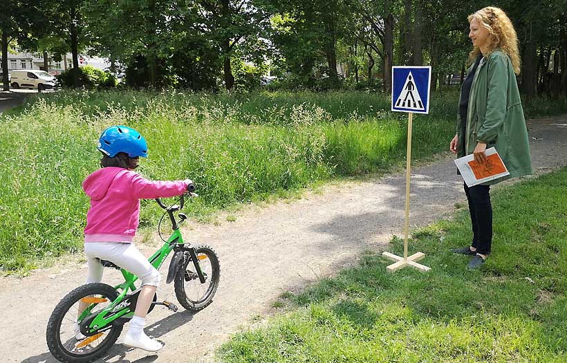 Kind übt Radfahren in einem Parkour und eine Erzieherschülerin der DPFA Leipzig erklärt, wie es geht.