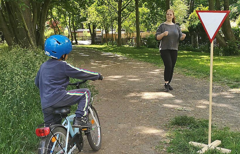 Ein Kind steht vor einem Vorfahrtsschild im Fahrradparkour und eine Erzieherschülerin der DPFA Leipzig erklärt, wie es geht.