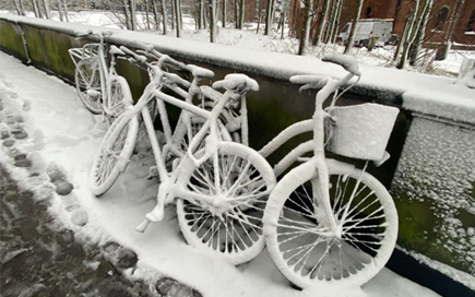 An einem verschneiten Gehweg steht ein Fahrrad, welches voller Schnee ist.